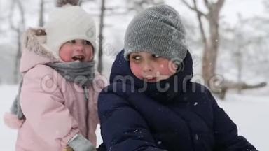 女儿帮助母亲在降雪时和儿子拉雪橇。 幸福的家庭在下雪的冬天滑雪。 可爱的小女孩